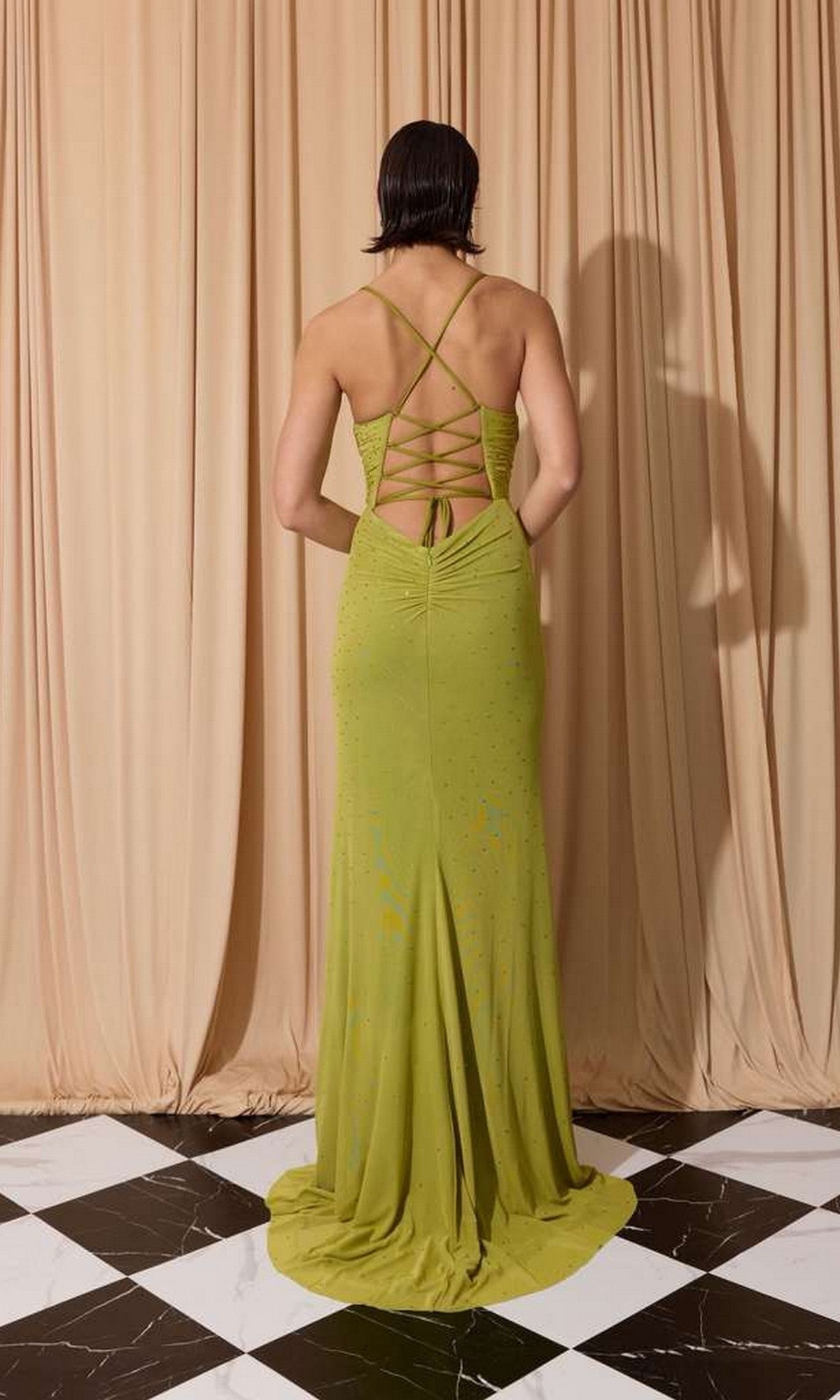 A person wearing the Spaghetti-Strap Long Formal Dress: Eureka EK187 stands on a black-and-white tiled floor in front of beige curtains.